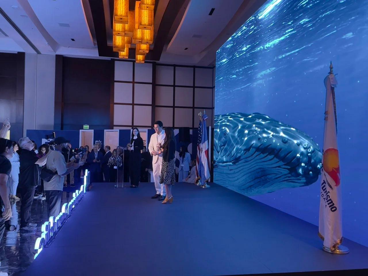 Dominican Republic Tourism Showcase: An underwater LED environment in Miami: a 3D whale crossing a stage wall and five towers, with a round LED bar in the middle of it.