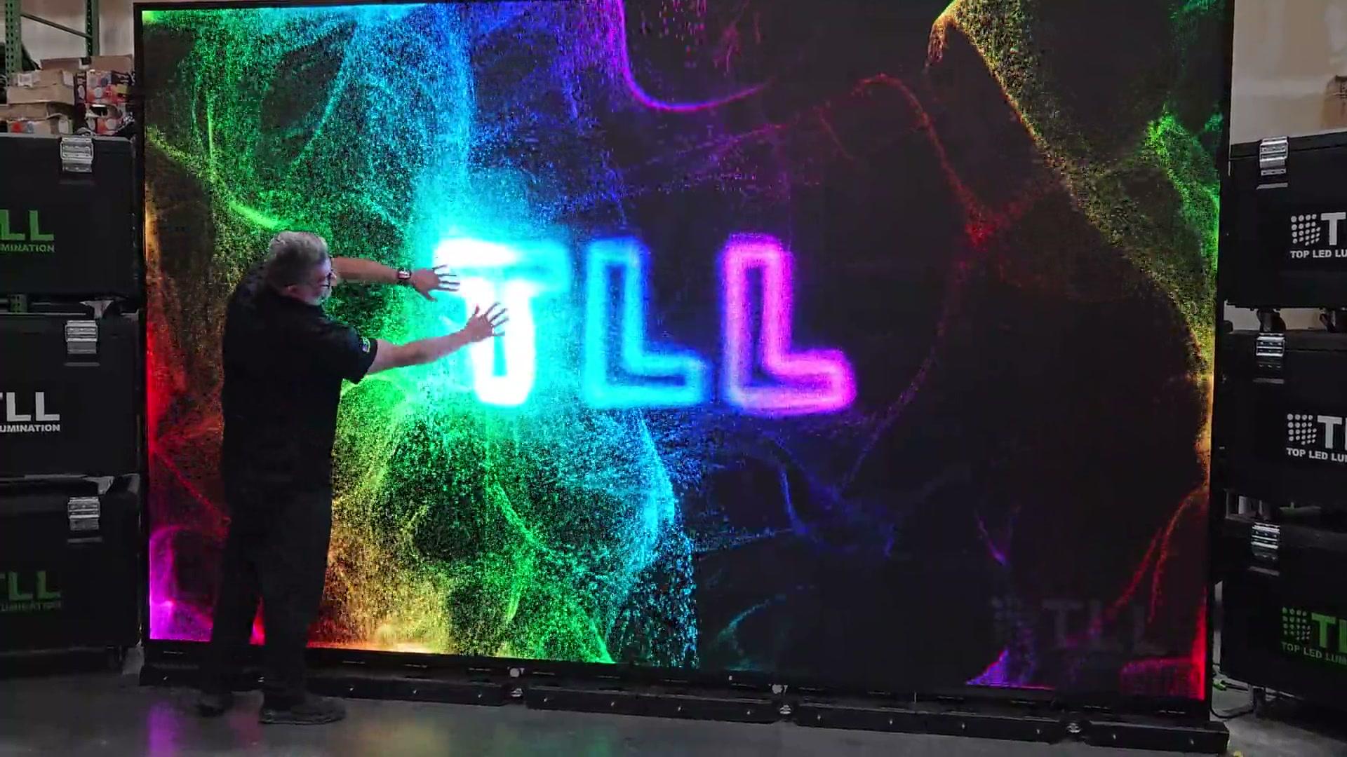 A glowing logo in the middle of a particle field on a large LED wall, with a person reaching into it